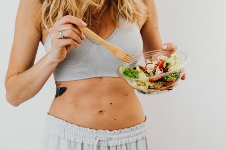 Young woman in sports attire holding a fresh salad bowl, promoting a healthy lifestyle.