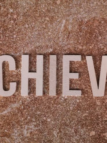 Wooden letters spelling 'ACHIEVE' on a textured brown surface, conveying motivation and success.