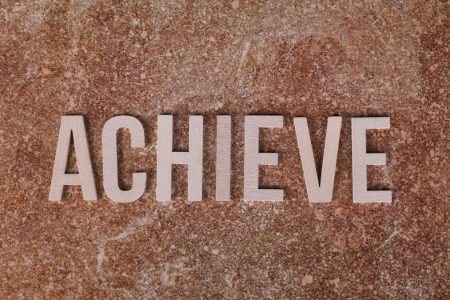 Wooden letters spelling 'ACHIEVE' on a textured brown surface, conveying motivation and success.