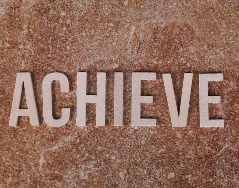 Wooden letters spelling 'ACHIEVE' on a textured brown surface, conveying motivation and success.